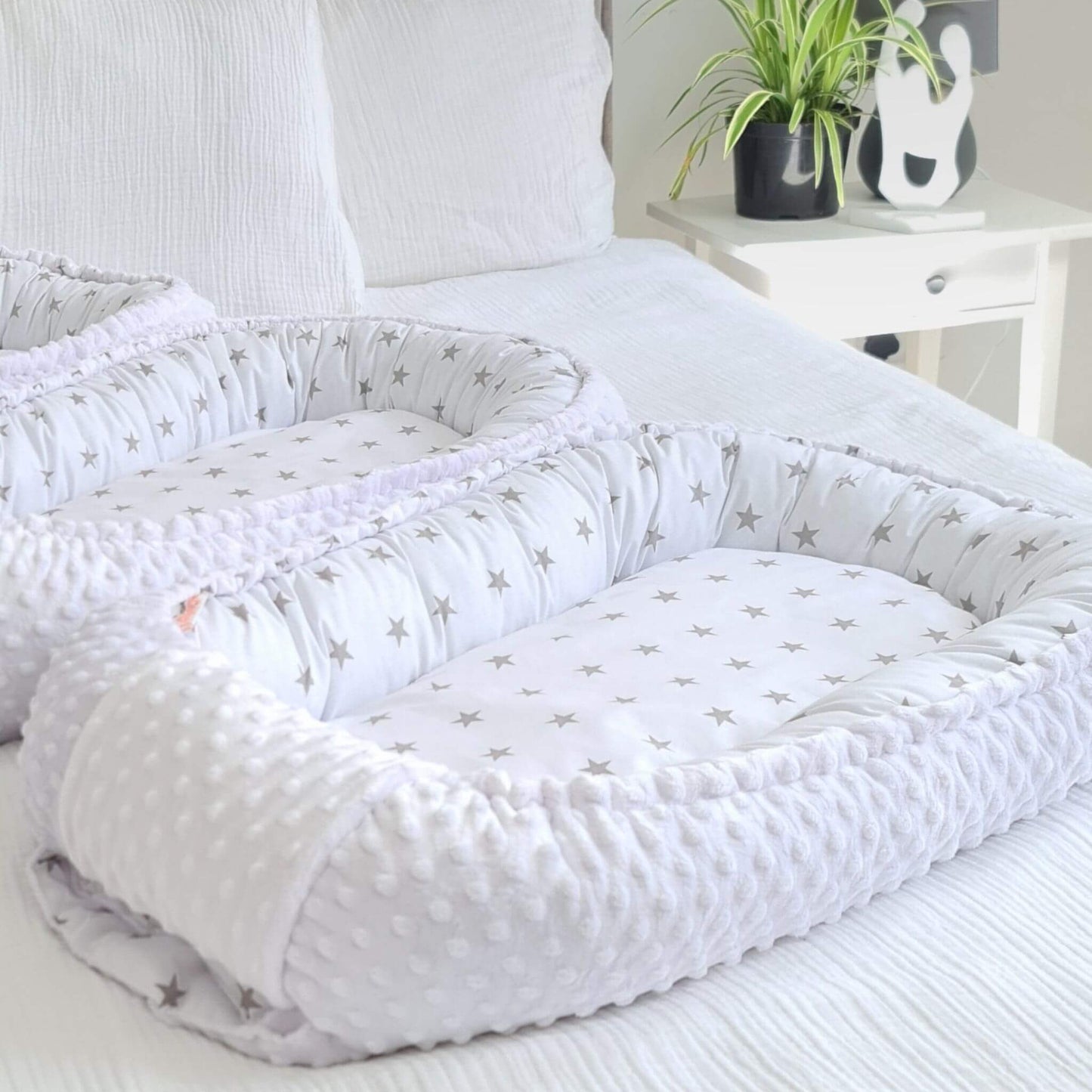 White crib bumper baby nest with star pattern on a bed in a bedroom setting.