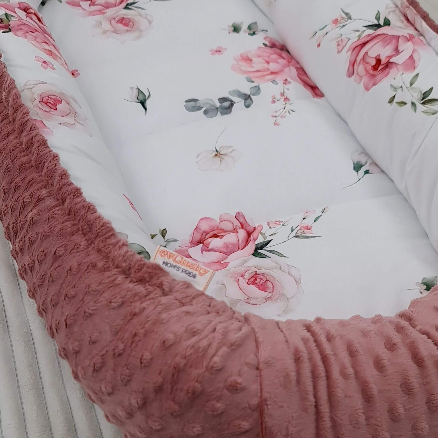 Side view of Blooming Rose XXL baby nest sleeping pod with pink plush bottom and rose pattern on white cotton