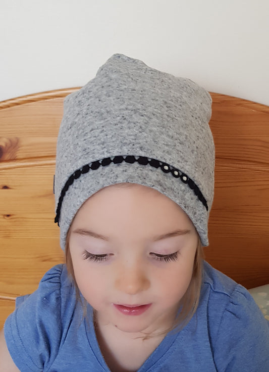 A child wearing a gray beanie hat with a dotted pattern around the edge.