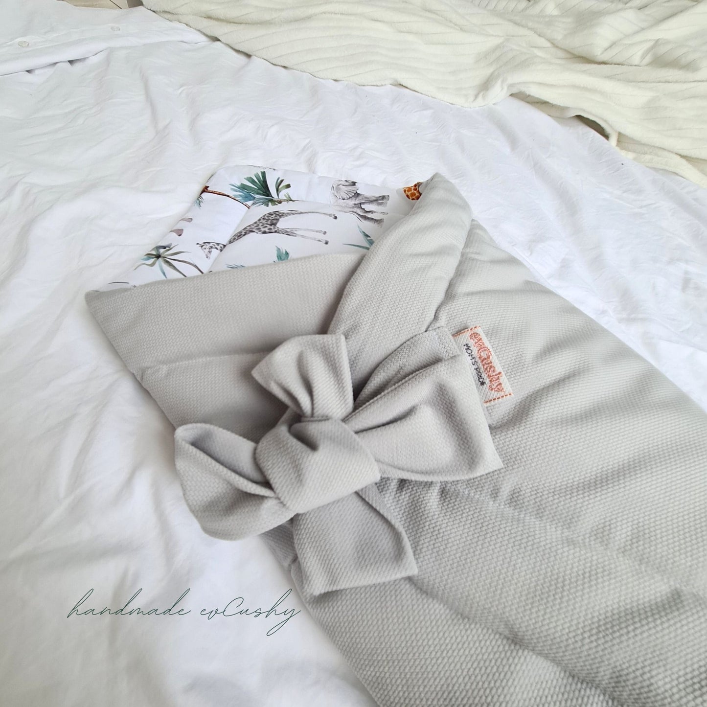 multi-functional 3-in-1 swaddle blanket, featuring a stylish grey exterior and a delightful safari animal pattern on the inside. It is elegantly tied with a bow for added charm.