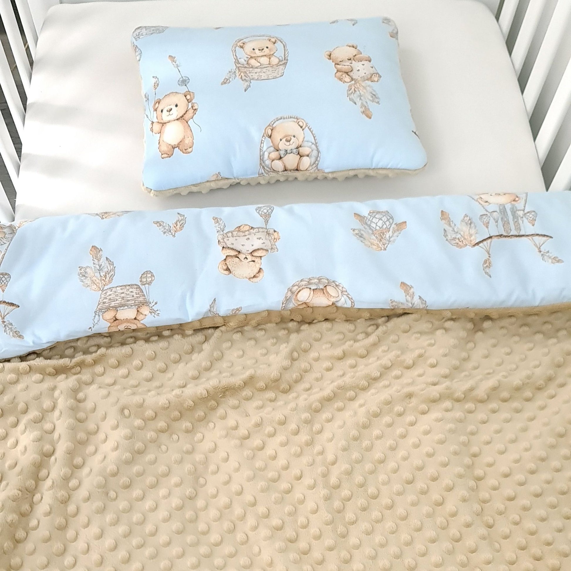 Baby crib set with teddy bear pattern on blue and beige fabric baby blanket and fillow in the crib showing both sides plain mokka plush and blue cotton with teddy bears