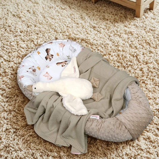 Baby nest with blanket and toy on a carpeted floor- evcushy baby sleeping pod 