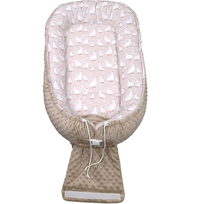 Baby nest with pink and white patterned top and beige bottom on a white background