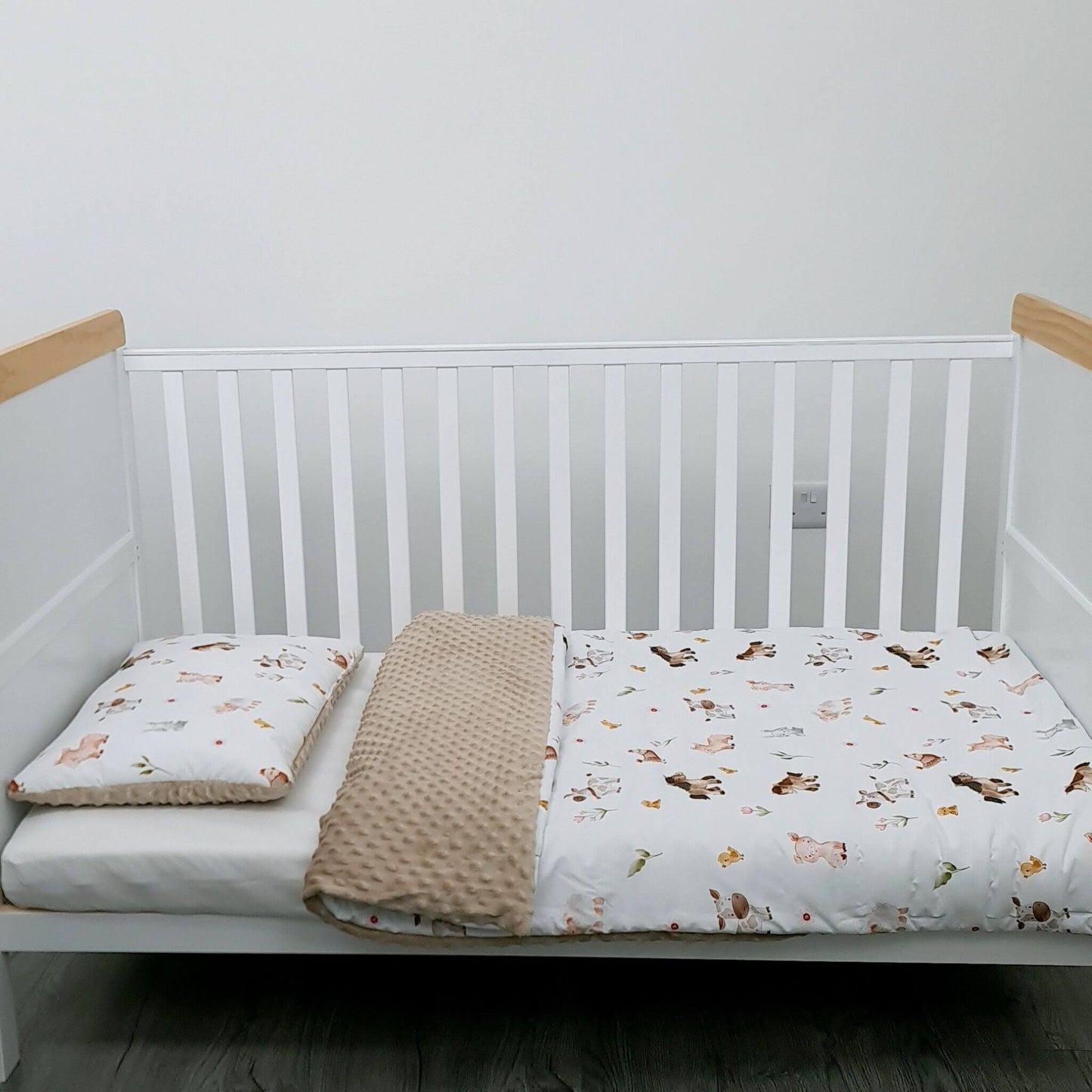 White crib with wooden bars, white mattress, beige blanket, and animal-patterned sheet on a plain background