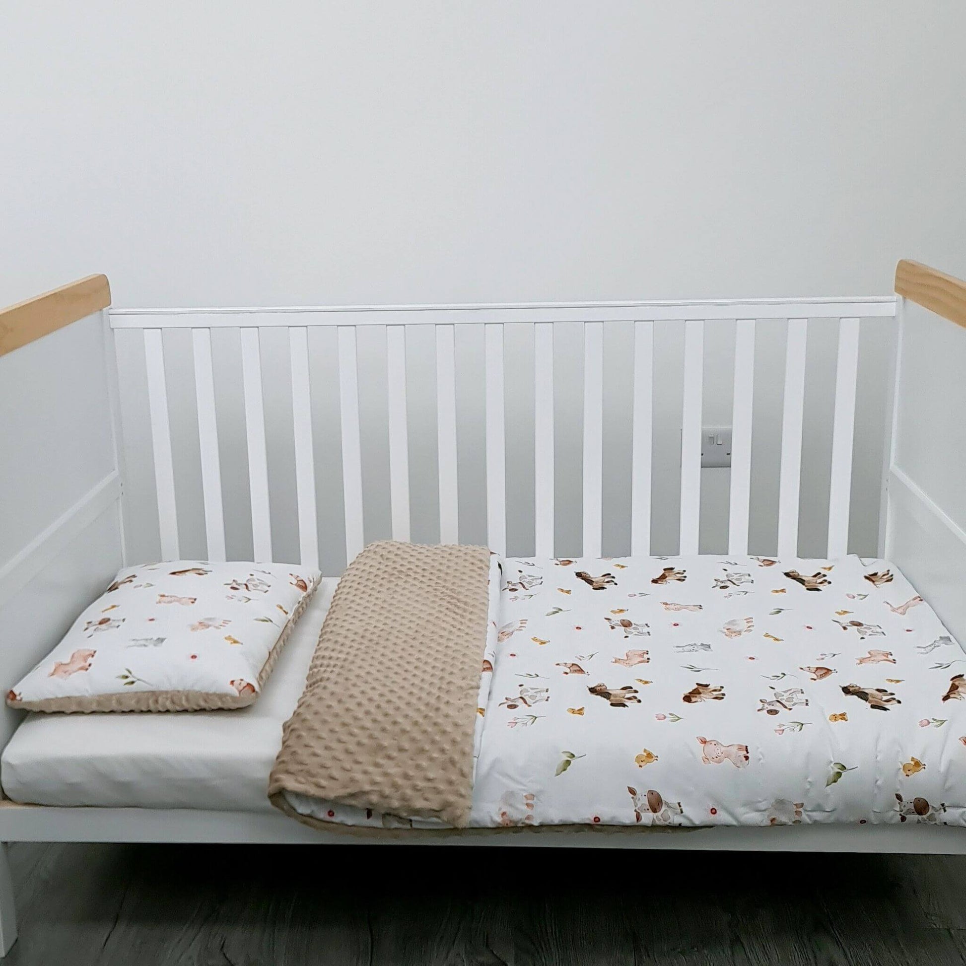 White crib with wooden bars, white mattress, beige blanket, and animal-patterned sheet on a plain background