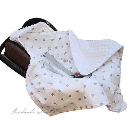 Image: A white car seat blanket with grey stars, featuring a convenient hood for added comfort and warmth.